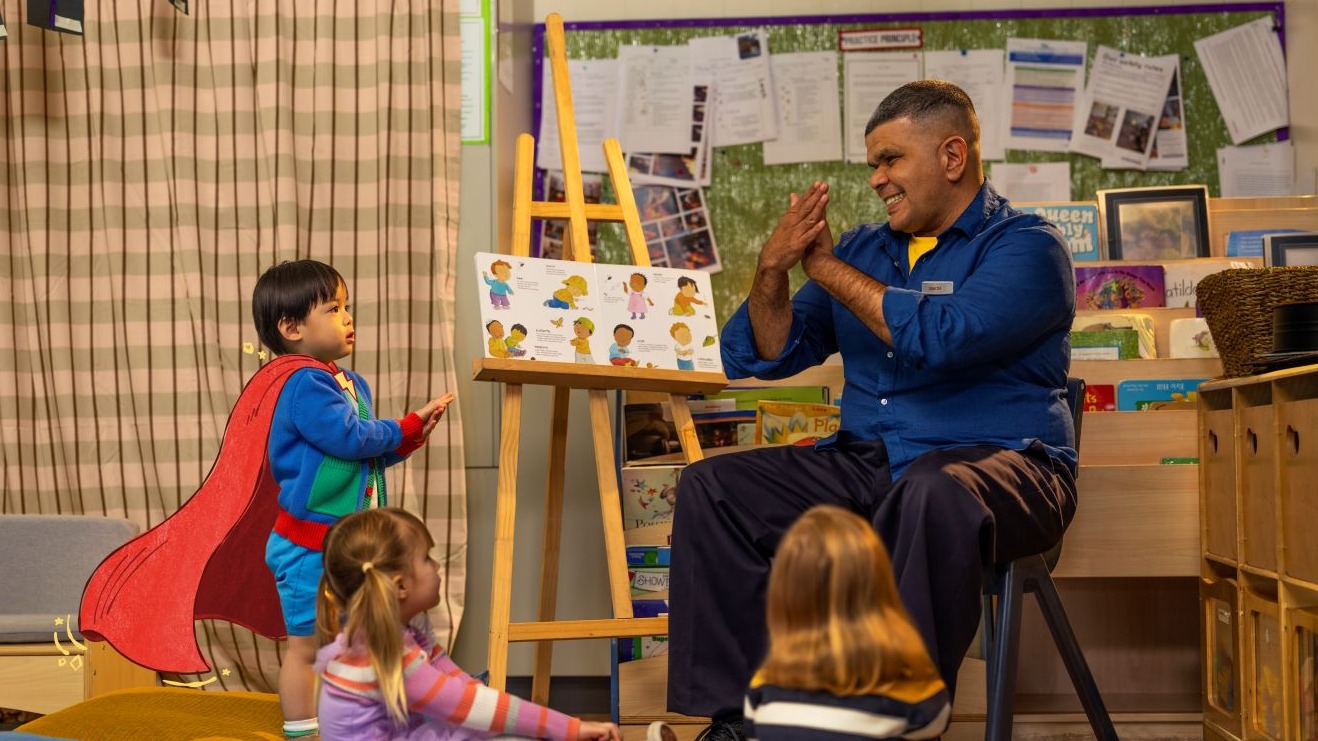 A male educator engaging with a 3-year-old student wearing an animated cape