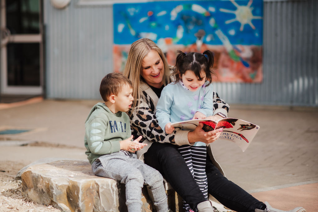 Two young children sit with an early childhood educator