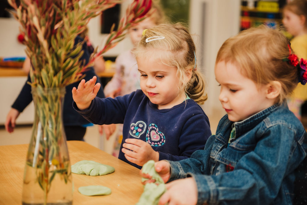 Two children at a table looking at and playing with playdough