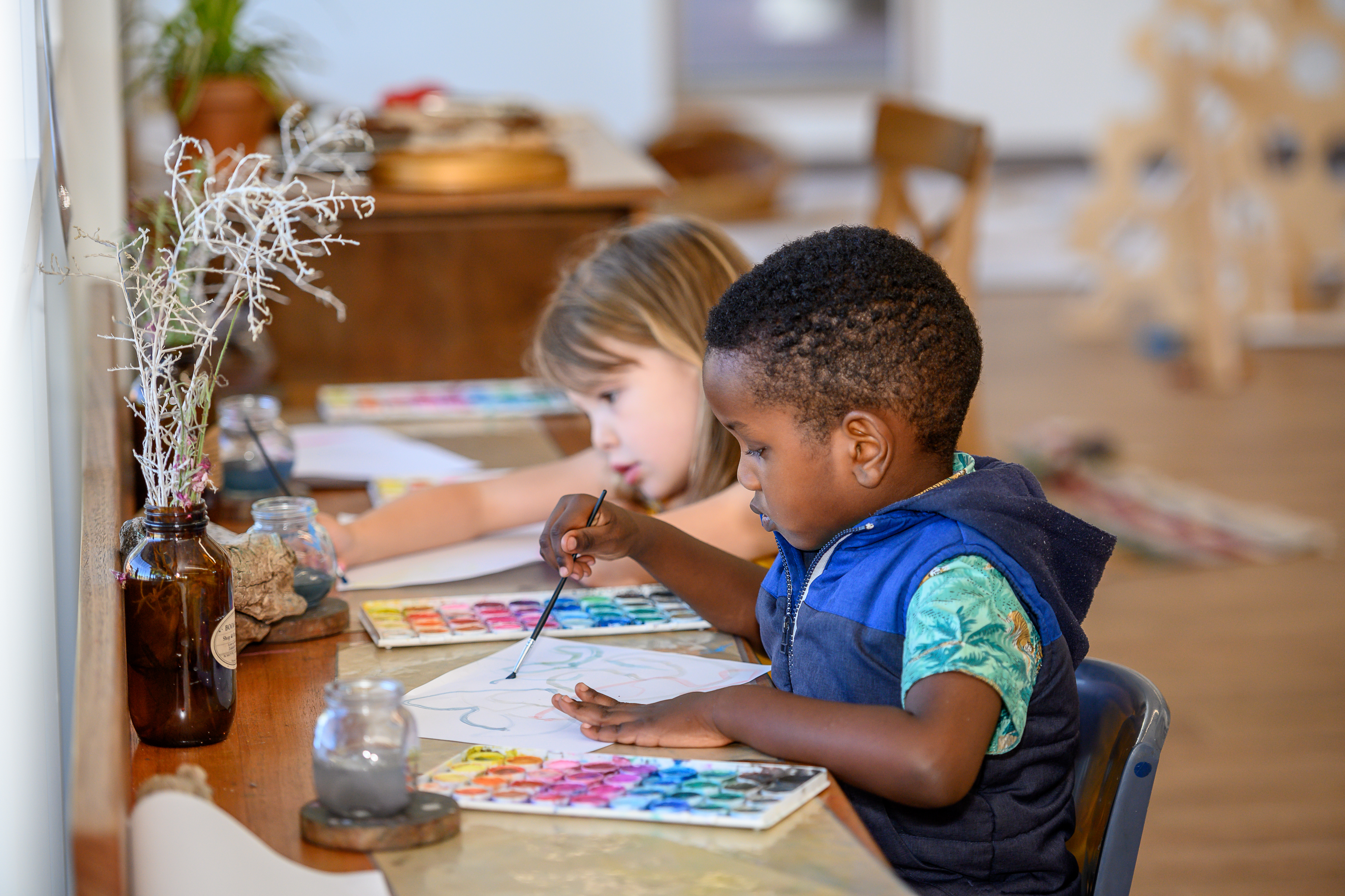 A boy in a blue vest is painting at a table